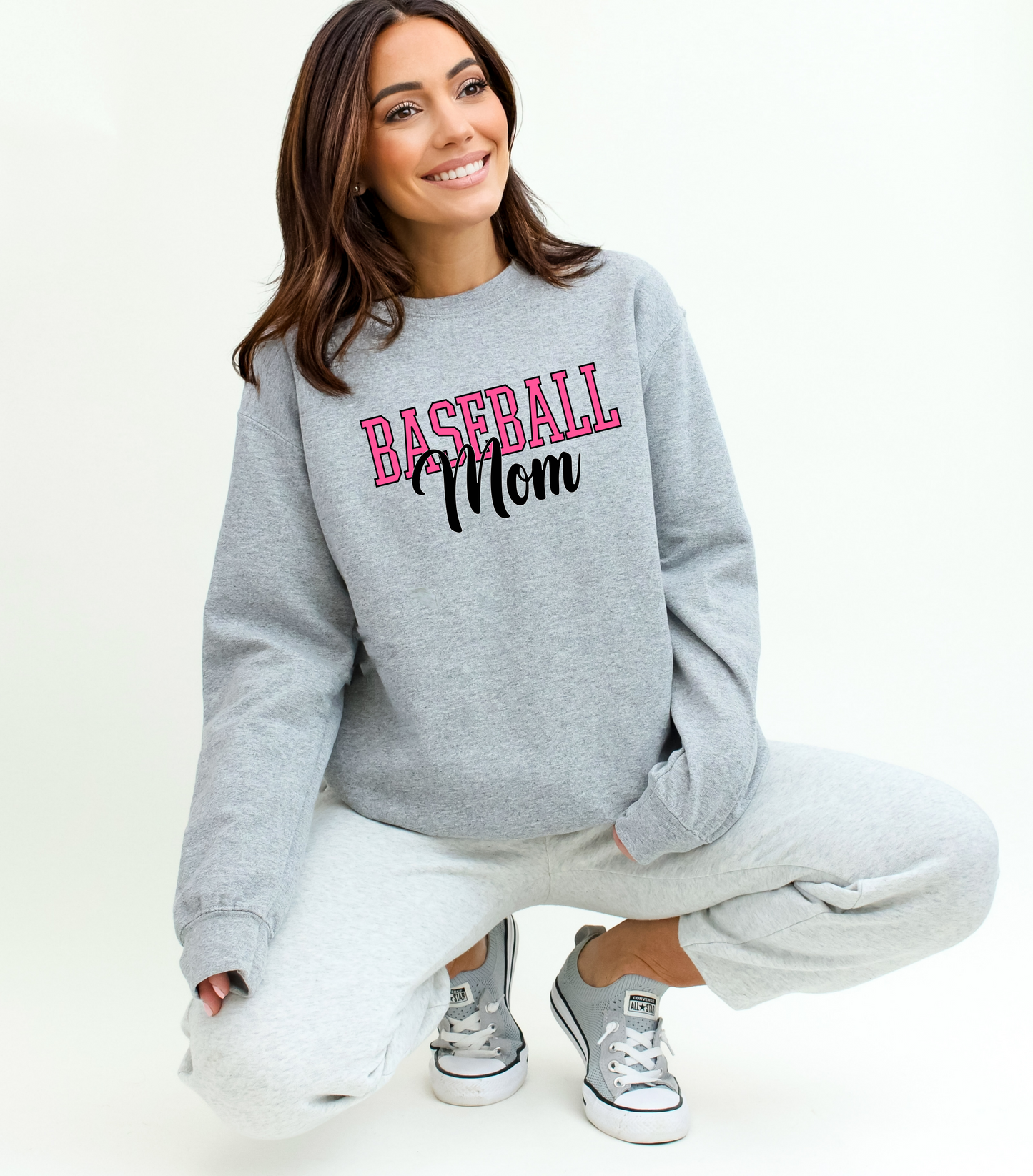 Woman wearing a gray sweatshirt with 'Baseball Mom' text, sitting on a white background