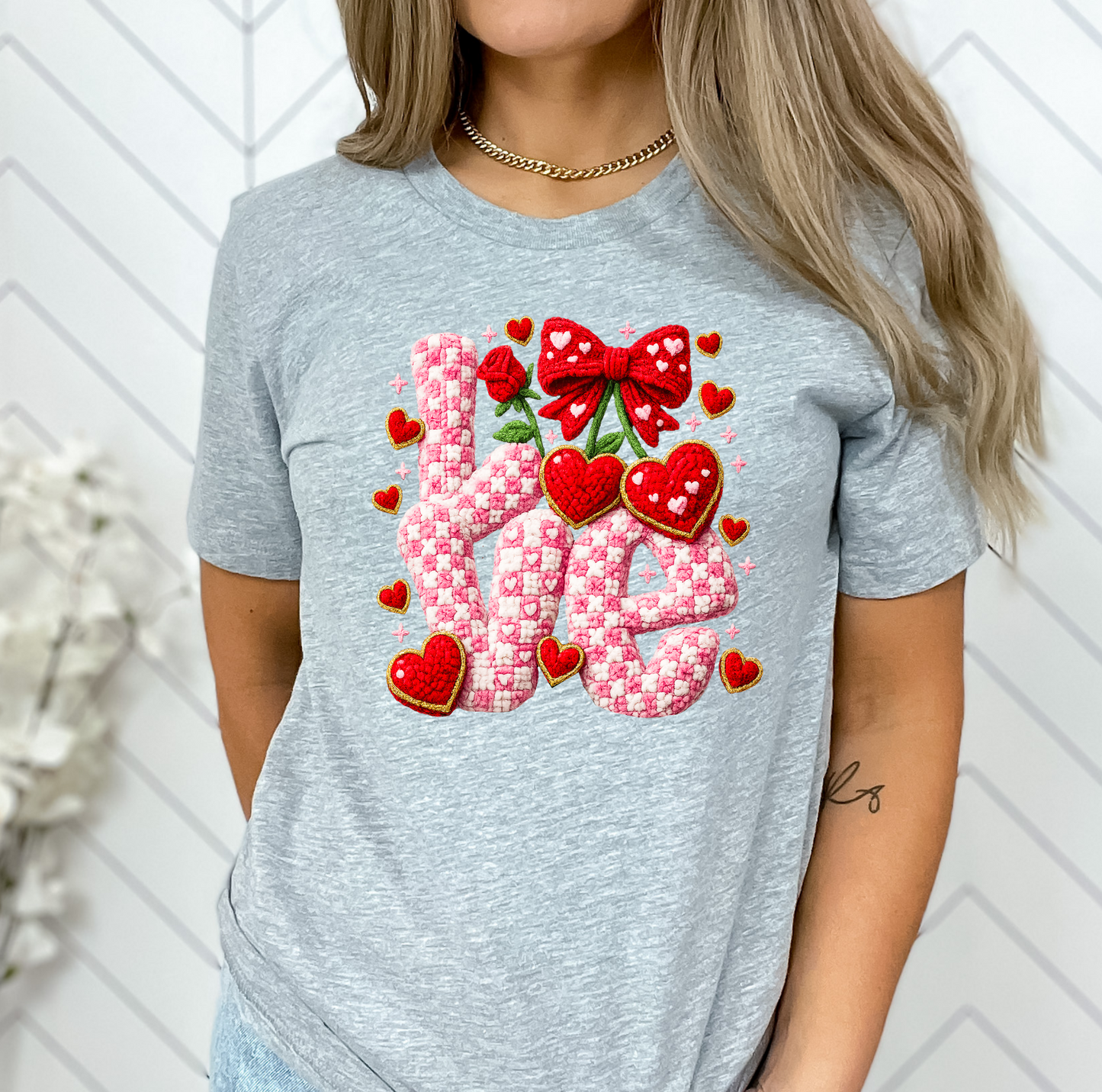 Person wearing a gray t-shirt with decorative text and graphics against a white wall.