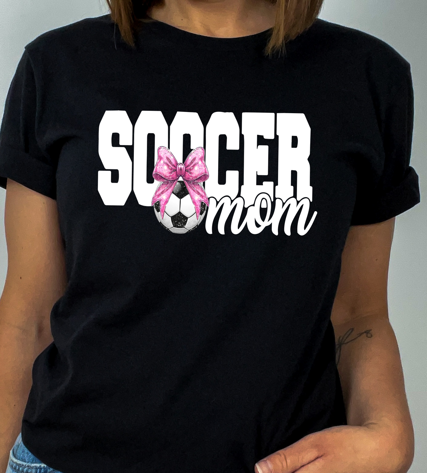 Person wearing a black t-shirt with 'Soccer Mom' text and a pink bow graphic.