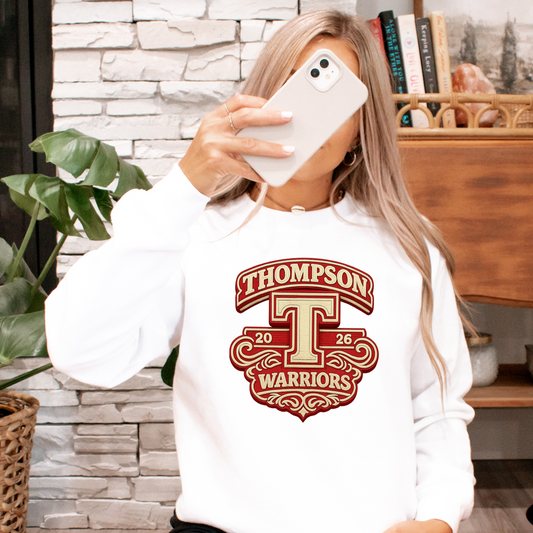 Person wearing a white sweatshirt with a school logo, sitting on the floor in a room with plants and a Victrola record player.